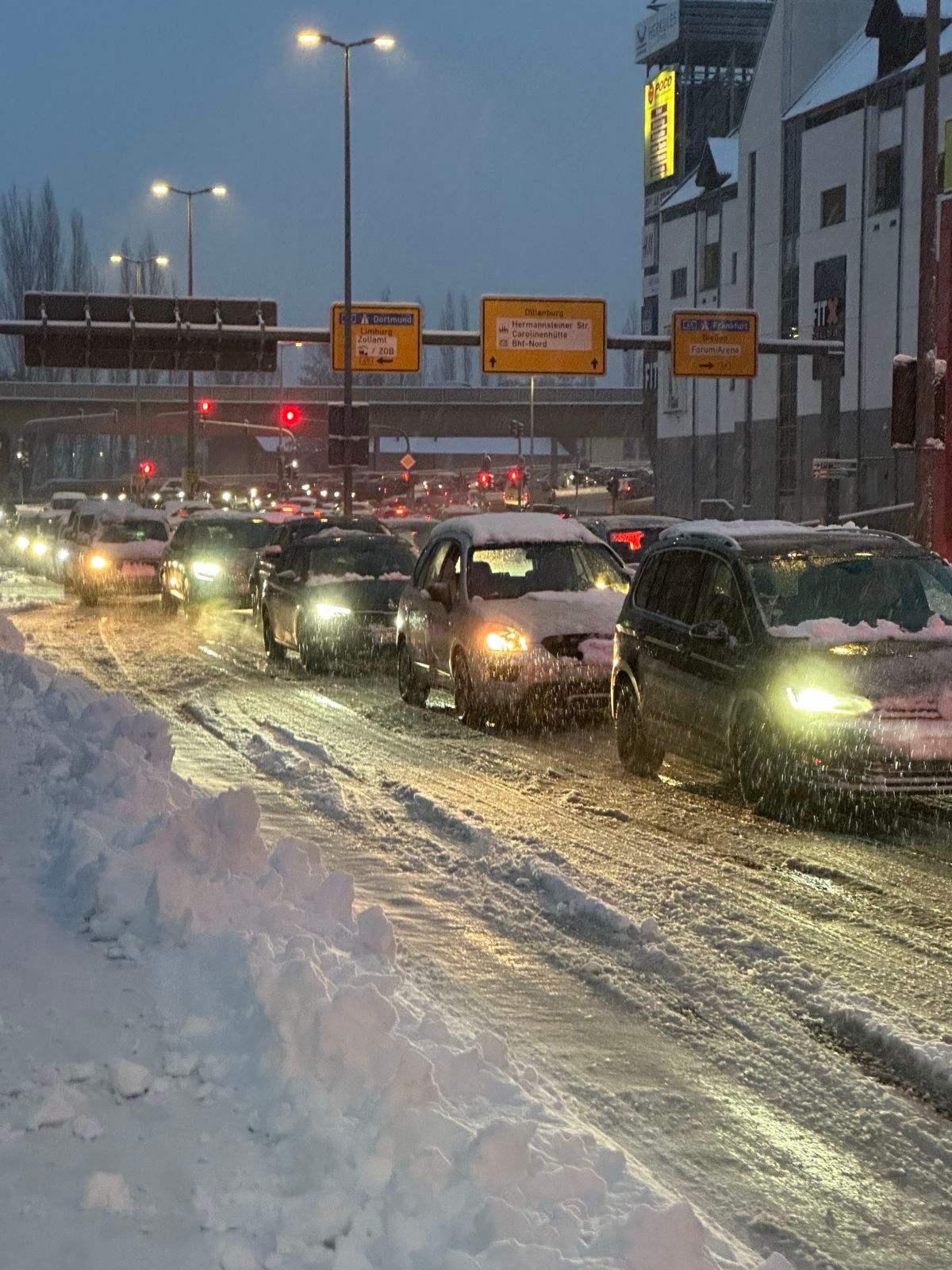 Mehrere Autos stehen im stockenden Verkehr auf einer schneebedeckten Straße bei Dämmerung