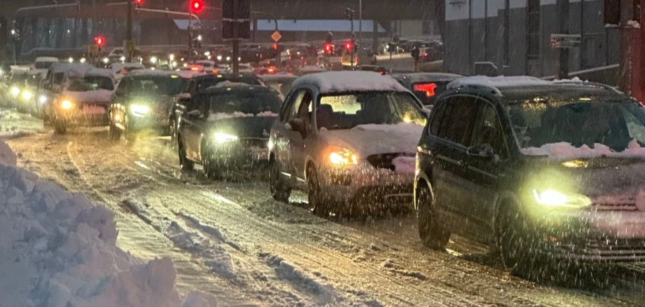 Mehrere Autos stehen im stockenden Verkehr auf einer schneebedeckten Straße bei Dämmerung