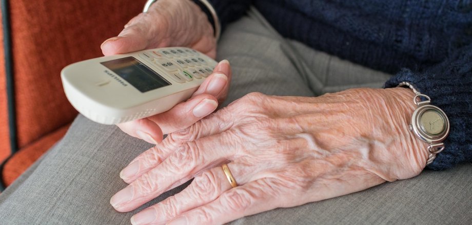 Älterer Mensch hält ein Telefon in der Hand.